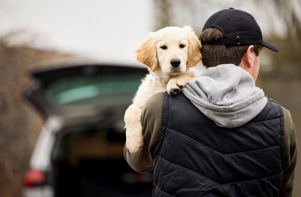 Man in ball cap holding puppy looking over his shoulder.